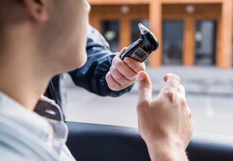 cropped view of policeman giving breathalyzer to driver in car, blurred foreground.