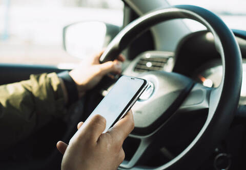 Handling your phone while driving. Close-up of a hand holding a phone and steering wheel of a car while driving.