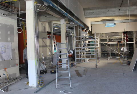 Auf dem großen Banner vor dem alten Rewe, der 2015 schloss, ist der künftige Innenbereich der neuen Markthalle zu sehen, auf dem rechten Bild der entstehende Verkaufsbereich der Bäckerei Raisch. Entlang des Lüftungskanals an der Decke, an dem hier gearbeitet wird, wird die Verkaufstheke stehen.