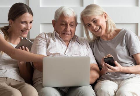 Happy older parents with adult daughter using electronic devices