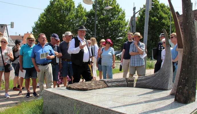 An der Skulptur „Waldenserperlen“ von Bildhauer Karl-Heinz Zöhner zeigt Eberhard Rivoir in Waldensertracht, wo das Freibad war. An der Skulptur „Waldenserperlen“ von Bildhauer Karl-Heinz Zöhner zeigt Eberhard Rivoir in Waldensertracht, wo das Freibad war. Nebenbei erzählt er vom vielseitigen Vereinsleben seinerzeit, zu dem der Radfahrverein, die Fußballmannschaft und die Bläsergruppe zählen.