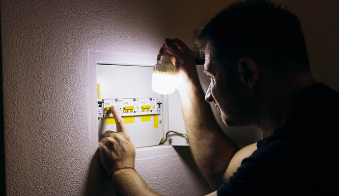 Die Schömberger müssen am Montag teilweise ohne Strom auskommen. Power outage. A man holds an LED lamp in front of an electrical panel.