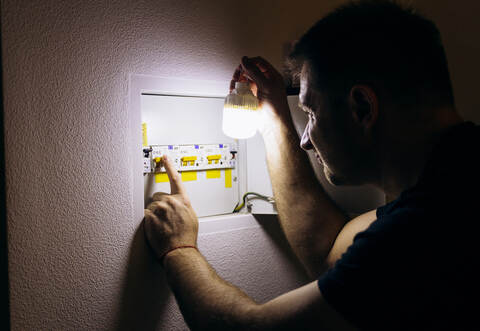 Power outage. A man holds an LED lamp in front of an electrical panel.