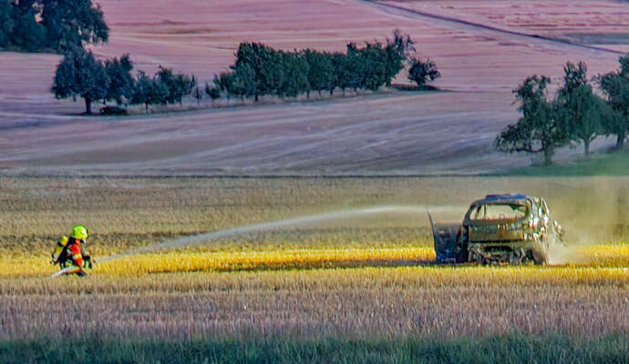 Das Auto wird auf dem Feld von einem Feuerwehrmann gelöscht.