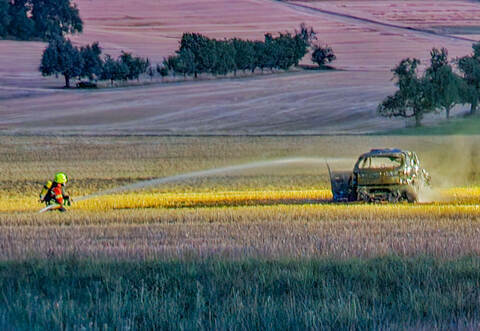 Das Auto wird auf dem Feld von einem Feuerwehrmann gelöscht.