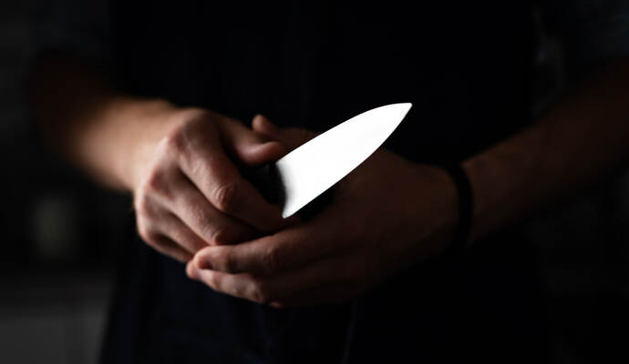 Ein 43-jähriger Mnan soll in Bretten mit einem Messer schwer verletzt worden sein. Man Holds Sharp Kitchen Knife in black room