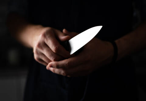 Man Holds Sharp Kitchen Knife in black room