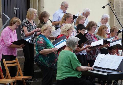 Auf den Stufen zum Seiteneingang der Kirche haben sich die Sänger der Stephanuskantorei aufgestellt, die Augen auf Ulrike Rothen gerichtet, die die Gesamtleitung innehat.