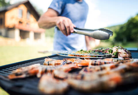 Unrecognizable man cooking seafood on a barbecue grill in the backyard.