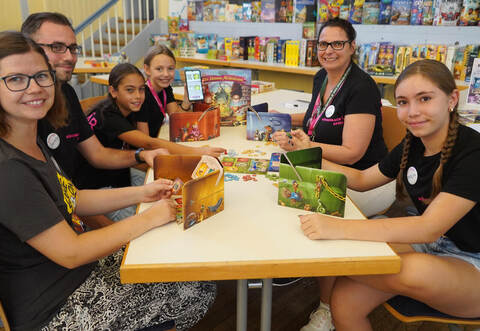 Zusammen mit einigen Kindern freuen sich Bianca Jung von Heidelbär Games, Benjamin Knab von den „Brettspielsuchties“ und Schulsozialarbeiterin Anke Burkhard (von links) über einen gelungenen Brettspieltag. Nico Roller