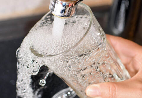 Eine Frau füllt ein Glas mit Trinkwasser aus dem Hahn