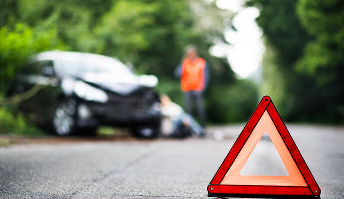 A close up of a red emergency triangle on the road in front of a car after an accident.