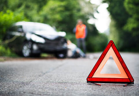 A close up of a red emergency triangle on the road in front of a car after an accident.