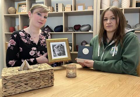 Jana Hinkelmann und Anubis-Filialbetreiberin Sandra Schmälzle (von links) mit der dezent gestalteten Urne für ihre Katze Happy, in der die Asche in der vertieften Rückwand des Bilderrahmens unauffällig Platz findet. Schmälzle hält einen Pfotenabdruck als Erinnerungsstück eines gestorbenen Tiers in der Hand .