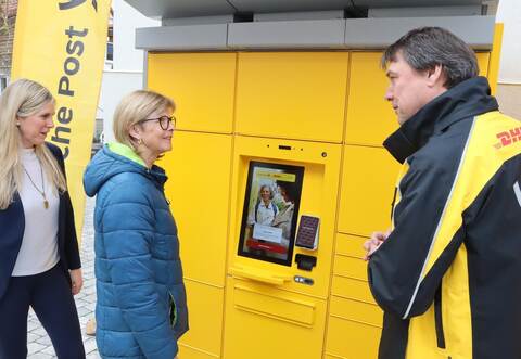 Martin Fichtner, Regionalbeauftragter der DHL Group (rechts) erklärt Postkundin Karin Glatthaar (Mitte) im Beisein von Bürgermeisterin Sabine Wagner (links) die Handhabung der neuen Poststation in Neuhausen Hamberg.