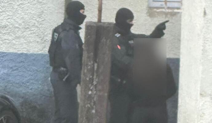 Anwohner beobachten im ersten Morgenlicht vermummte Polizisten an einem der durchsuchten Objekte.