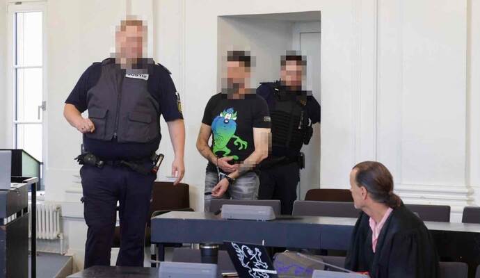 Der Angeklagte wird von Justizbeamten in Handschellen vorgeführt.