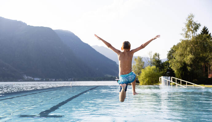 Active teenager boy jumping into an outdoor pool in the Alps. Summer holiday concept