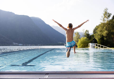 Active teenager boy jumping into an outdoor pool in the Alps. Summer holiday concept