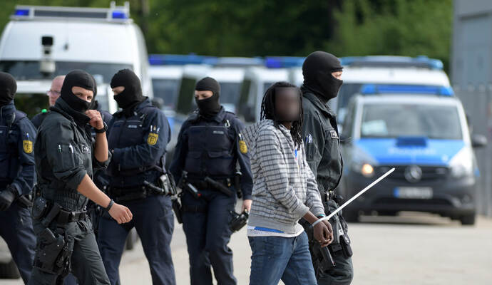 In der Landeserstaufnahmeeinrichtung für Flüchtlinge (LEA) wird ein gefesselter Mann von maskierten Polizisten abgeführt.