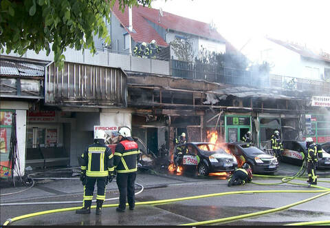 Als die Feuerwehr eintraf, standen die komplette Ladenzeile sowie mehrere Fahrzeuge in Flammen.