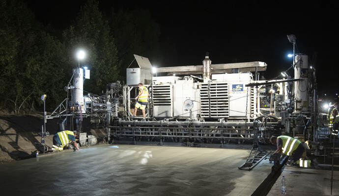 Betonfertiger: diese 14-Meter-Maschine betoniert die Fahrbahn rund um die Uhr mit einem Meter pro Minute. Es entsteht ein besonders haltbarer Straßenbelag, der bei hohem Schwerverkehrsanteil sehr beständig ist.