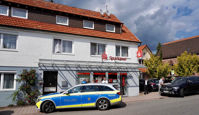 Spurensuche vor der Sparkasse in der Grunbacher Ortsmitte: Am Dienstagnachmittag wurde die Bank ausgeraubt. Mehr als 20 Polizisten waren vor Ort im Einsatz. Unmittelbar hinter der Kirche (rechts) beginnt der Friedhof, auf dem sich die Täter Stunden vor ihrem Überfall aufgehalten haben sollen.