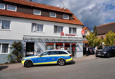 Spurensuche vor der Sparkasse in der Grunbacher Ortsmitte: Am Dienstagnachmittag wurde die Bank ausgeraubt. Mehr als 20 Polizisten waren vor Ort im Einsatz. Unmittelbar hinter der Kirche (rechts) beginnt der Friedhof, auf dem sich die Täter Stunden vor ihrem Überfall aufgehalten haben sollen.