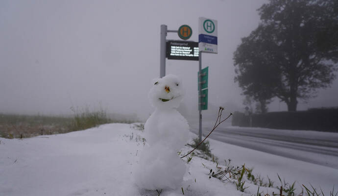 Ein kleiner Schneemann steht neben einer Bushaltestelle neben einer weiß verschneiten Straße auf dem Feldberg im Schwarzwald.