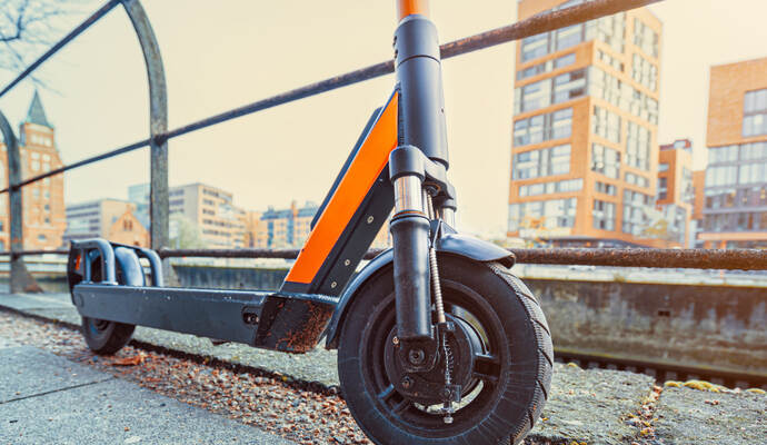 Orange colored e-scooter front perspective view parked outdoor on pavement of urban city scene