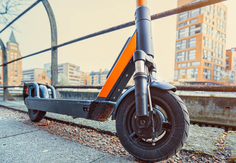Orange colored e-scooter front perspective view parked outdoor on pavement of urban city scene