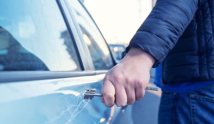 Bad guy scratching the car door with a key in the parking lot on the street. Damage of property from revenge for treason or betr