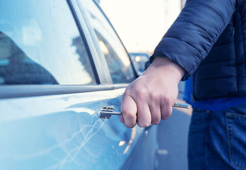 Bad guy scratching the car door with a key in the parking lot on the street. Damage of property from revenge for treason or betr