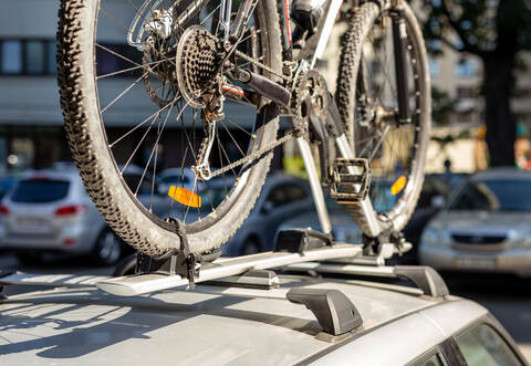 Close-up bicycle on car roof rack railing at outdoor parking. Vehicle with mounted bike on rooftop. Active sport touristic trip 