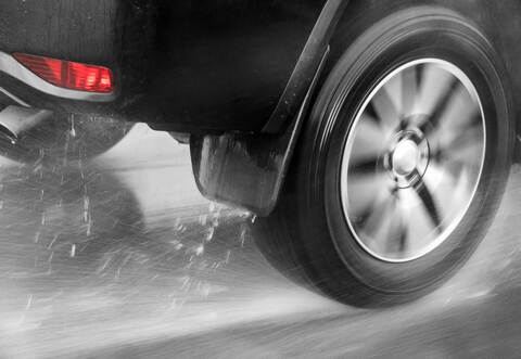 Detail of the rear wheel of a car driving in the rain on a wet road. Aquaplaning in road traffic.