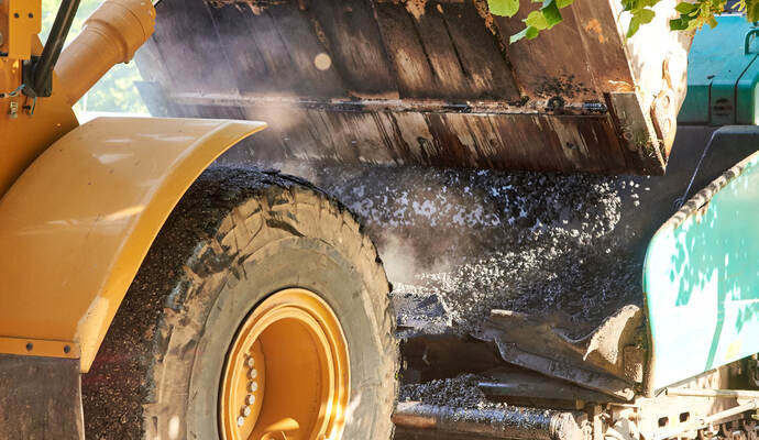 Das umweltgefährdende Gemisch wurde am Dienstagmorgen an einem Parkplatz entlang der Landesstraße gefunden. Bucket tractor pours hot asphalt into a grader, construction of a new road, material for road construction close-up.