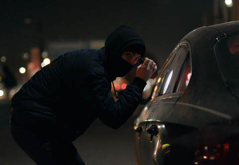 Robber man checking breaking entering alarm shines a flashlight in a car stealing at night crime male thief illegal theft stolen
