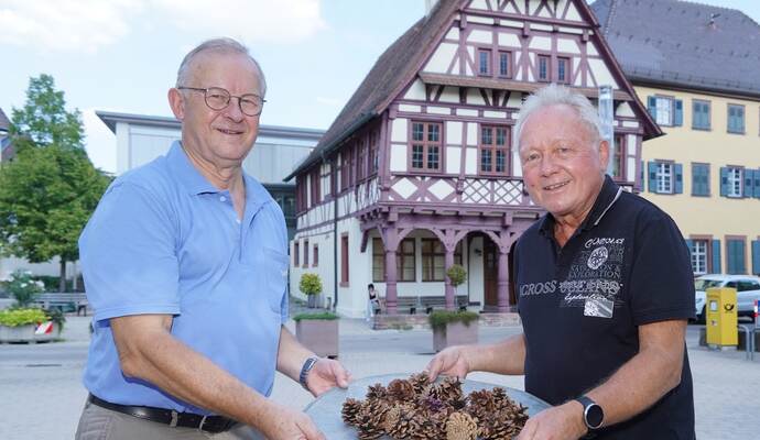 Hoffen auf viele Besucher: Bernhard Peichl und Peter Helmling gehören dem Organisationsteam fürs Dorffest an (von links). In den Händen halten sie Tannenzapfen für den traditionellen Hobbeles-Lauf. Foto: Roller