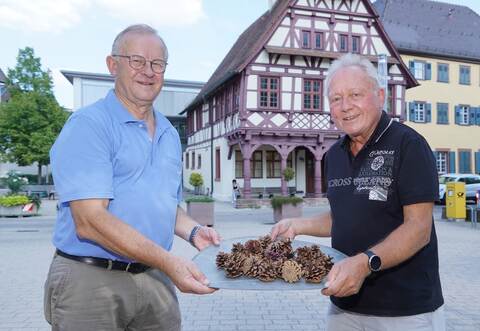 Hoffen auf viele Besucher: Bernhard Peichl und Peter Helmling gehören dem Organisationsteam fürs Dorffest an (von links). In den Händen halten sie Tannenzapfen für den traditionellen Hobbeles-Lauf. Foto: Roller