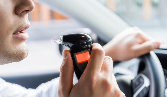 Zwei Promille zeigte der Alkomat an. partial view of man blowing into breathalyzer while sitting in car, blurred background.