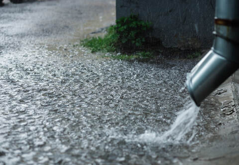 Rain water flowing from a metal downspout during a heavy rain. concept of protection against heavy rains