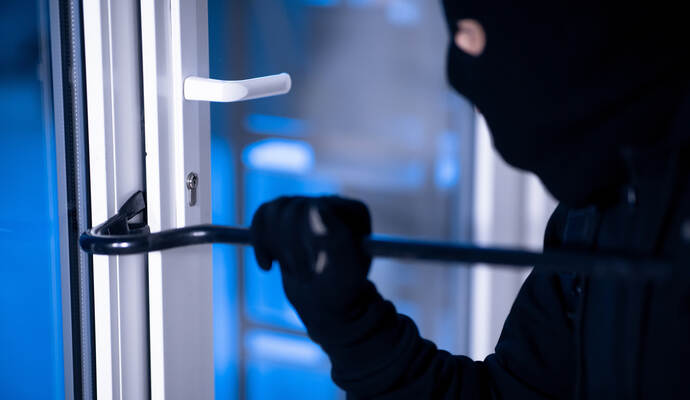 Robber in black balaclava cracking door with the crowbar