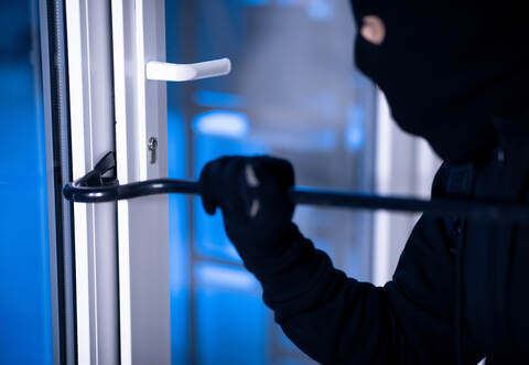 Robber in black balaclava cracking door with the crowbar
