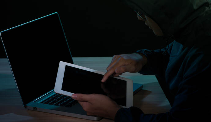 Im Laufe der Unterhaltung übersandte die Unbekannte dem Mann laut Polizei Nacktfotos, die angeblich die Chatpartnerin zeigten. Hooded cyber crime hacker using digital tablet internet hacking in to cyberspace