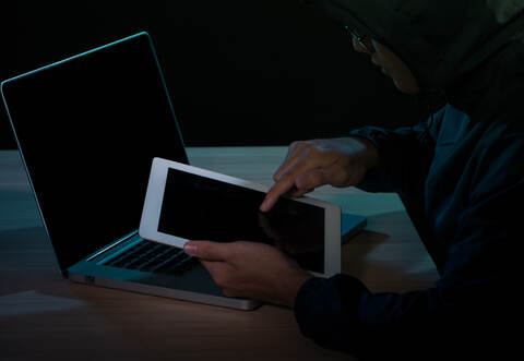 Hooded cyber crime hacker using digital tablet internet hacking in to cyberspace