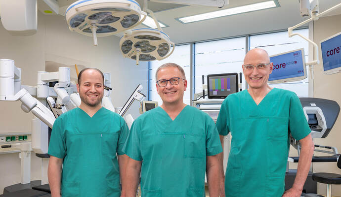 Stellen im „Urologischen Forum“ der „Goldstadt Privatklinik“ über eine Videokonferenz Roboter-assistierte Operationen zum Thema Prostatakrebs vor: (von rechts) OP-Robotik-Pionier Jörn H. Witt, der Ärztliche Direktor der Klinik, Sven Lahme, und Oberarzt Alaa Benchi. Rechts erkennt man die Steuerkonsole und links die Arme des Roboters. Bernhard Friese Stellen im „Urologischen Forum“ der „Goldstadt Privatklinik“ über eine Videokonferenz Roboter-assistierte Operationen zum Thema Prostatakrebs vor: (von rechts) OP-Robotik-Pionier Jörn H. Witt, der Ärztliche Direktor der Klinik, Sven Lahme, und Oberarzt Alaa Benchi. Rechts erkennt man die Steuerkonsole und links die Arme des Roboters. Bernhard Friese
