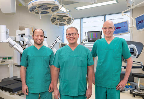 Stellen im „Urologischen Forum“ der „Goldstadt Privatklinik“ über eine Videokonferenz Roboter-assistierte Operationen zum Thema Prostatakrebs vor: (von rechts) OP-Robotik-Pionier Jörn H. Witt, der Ärztliche Direktor der Klinik, Sven Lahme, und Oberarzt Alaa Benchi. Rechts erkennt man die Steuerkonsole und links die Arme des Roboters.   Bernhard Friese