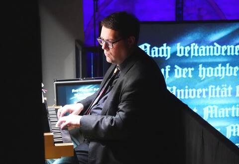Andreas Benz sitzt an der Orgel, während hinter ihm der Luther-Film über die Leinwand flimmert.