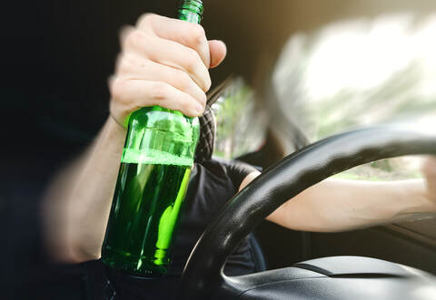 Close-up of a bottle of Alcohol in the driver hand at the wheel of car. Alcohol driving concept