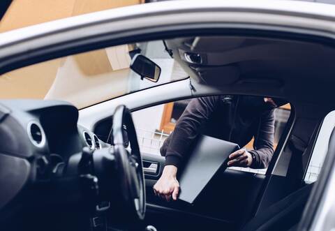 Masked thief in a balaclava stealing laptop computer